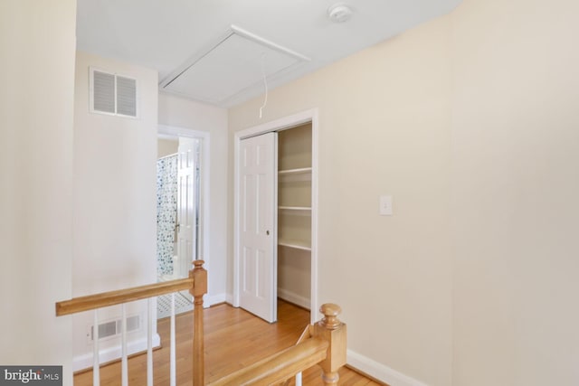 hallway featuring baseboards, visible vents, attic access, and light wood-style floors