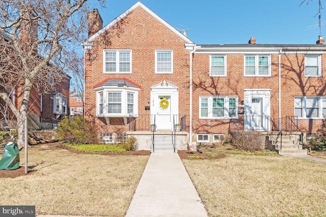 townhome / multi-family property with brick siding, a chimney, and a front yard