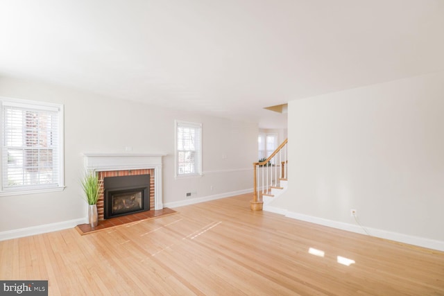 unfurnished living room featuring light wood finished floors, stairway, a brick fireplace, and baseboards