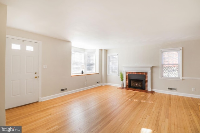 unfurnished living room featuring light wood-type flooring, visible vents, and a healthy amount of sunlight