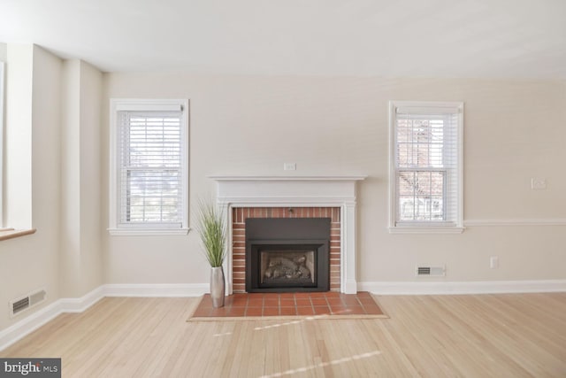 unfurnished living room with visible vents, a brick fireplace, and wood finished floors