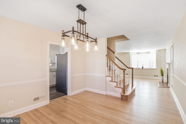 unfurnished dining area with light wood-type flooring, baseboards, visible vents, and stairway