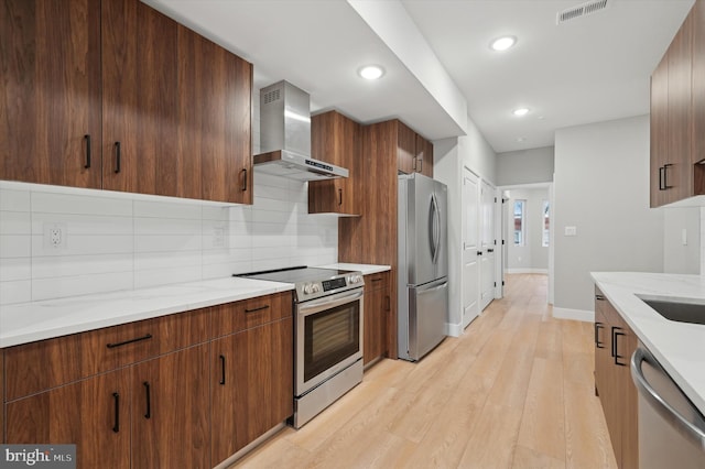 kitchen featuring backsplash, light hardwood / wood-style flooring, wall chimney exhaust hood, light stone counters, and stainless steel appliances