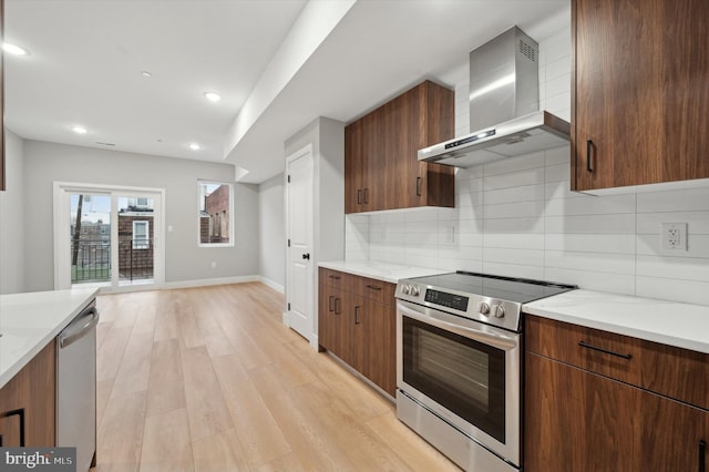 kitchen featuring decorative backsplash, light stone countertops, light wood-type flooring, wall chimney exhaust hood, and stainless steel appliances