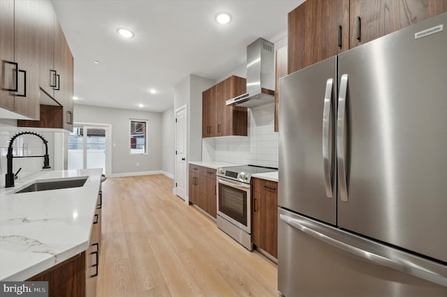 kitchen with sink, wall chimney range hood, tasteful backsplash, light hardwood / wood-style flooring, and appliances with stainless steel finishes