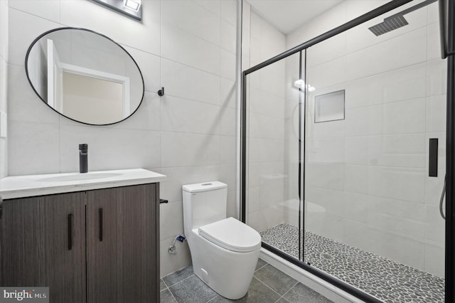 bathroom featuring tile patterned floors, toilet, vanity, a shower with shower door, and tile walls