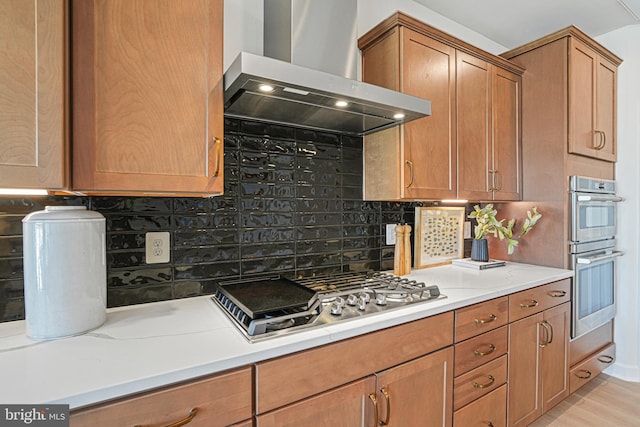 kitchen with appliances with stainless steel finishes, wall chimney range hood, backsplash, and light wood-type flooring