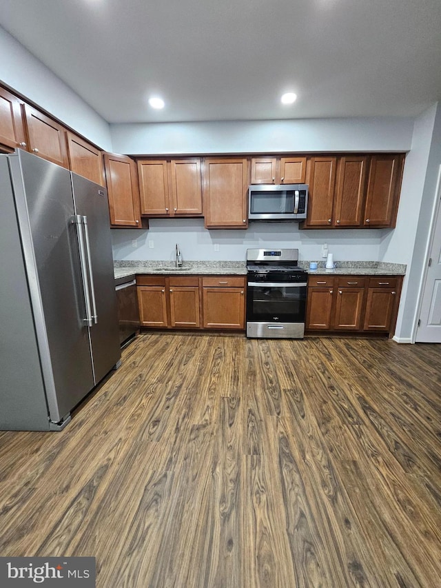 kitchen with sink, dark wood-type flooring, stainless steel appliances, and light stone countertops