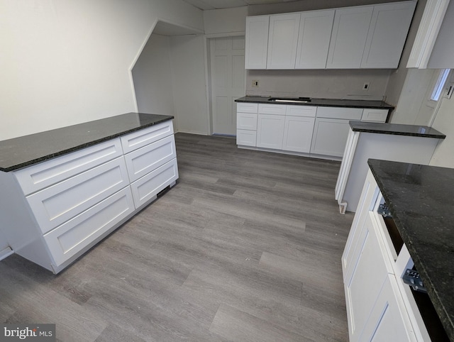 kitchen with white cabinets, sink, light hardwood / wood-style floors, and dark stone countertops