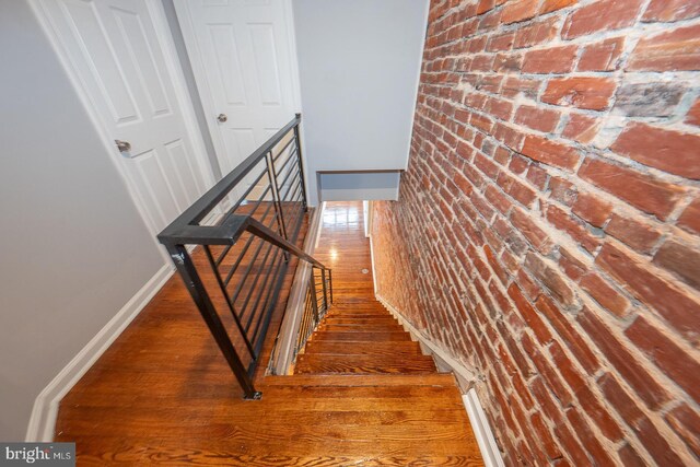 staircase with hardwood / wood-style floors and brick wall