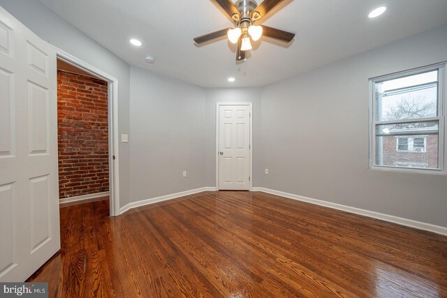 spare room featuring ceiling fan, dark wood-type flooring, and brick wall