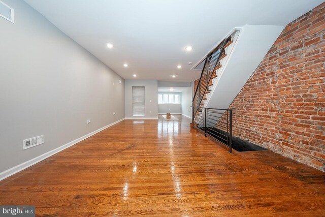 unfurnished living room with hardwood / wood-style flooring and brick wall