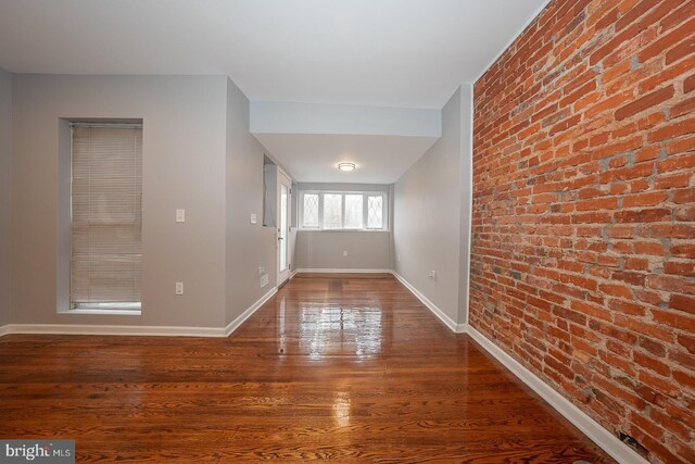 unfurnished room with hardwood / wood-style floors and brick wall