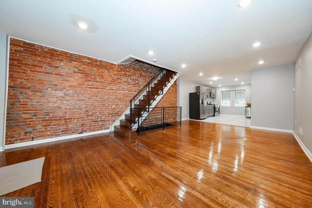 unfurnished living room with brick wall and light hardwood / wood-style flooring