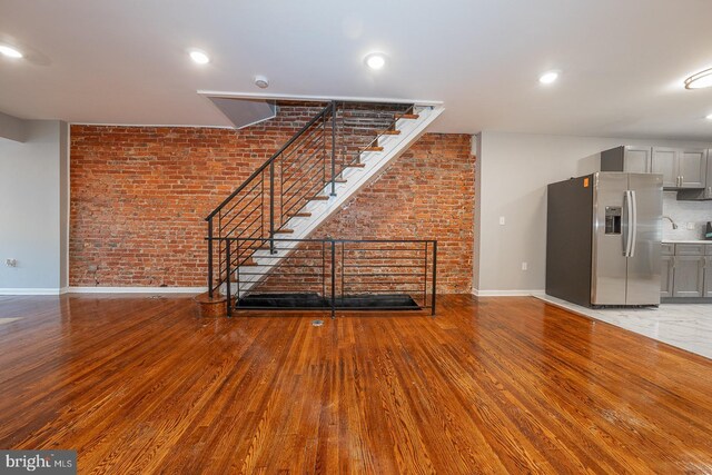 unfurnished living room featuring hardwood / wood-style floors and brick wall