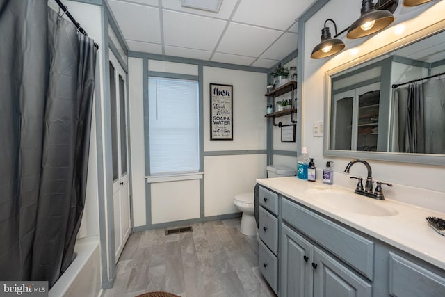 full bathroom featuring a drop ceiling, vanity, hardwood / wood-style flooring, shower / bathtub combination with curtain, and toilet