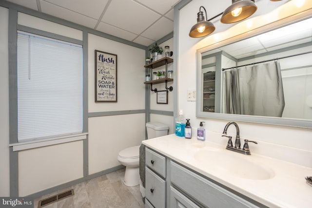 bathroom featuring a drop ceiling, toilet, walk in shower, and vanity