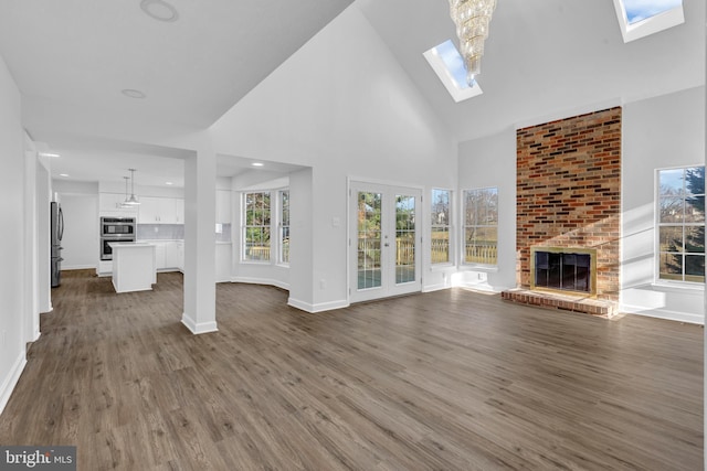 unfurnished living room with french doors, dark hardwood / wood-style flooring, a skylight, high vaulted ceiling, and a fireplace