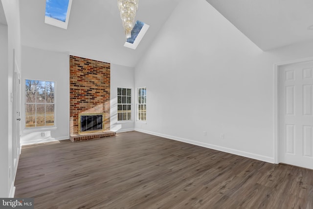 unfurnished living room featuring a brick fireplace, dark hardwood / wood-style flooring, a skylight, and high vaulted ceiling