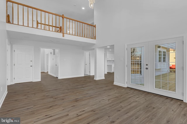 unfurnished living room featuring french doors, a towering ceiling, and wood-type flooring