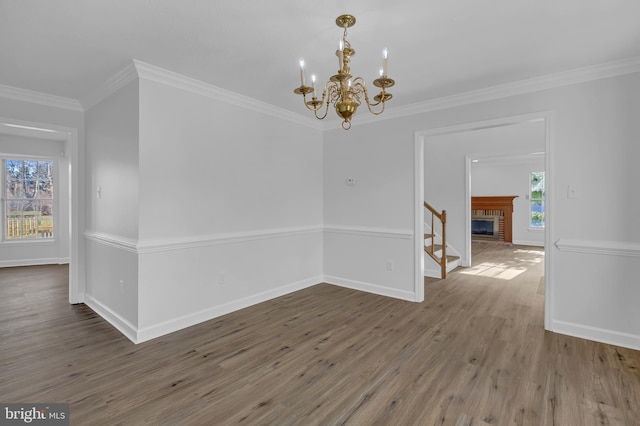 unfurnished room with a brick fireplace, hardwood / wood-style flooring, an inviting chandelier, and crown molding