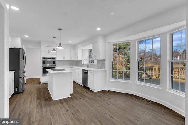 kitchen with appliances with stainless steel finishes, decorative light fixtures, white cabinetry, dark hardwood / wood-style floors, and a kitchen island