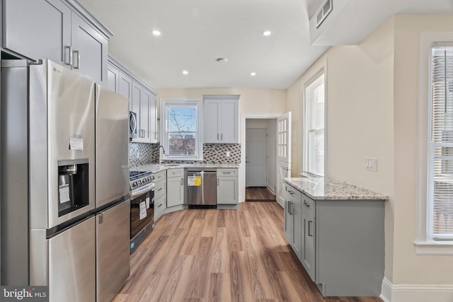 kitchen featuring appliances with stainless steel finishes, light hardwood / wood-style floors, light stone counters, and gray cabinetry