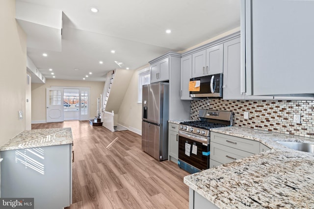 kitchen featuring appliances with stainless steel finishes, backsplash, light stone counters, light hardwood / wood-style flooring, and gray cabinets