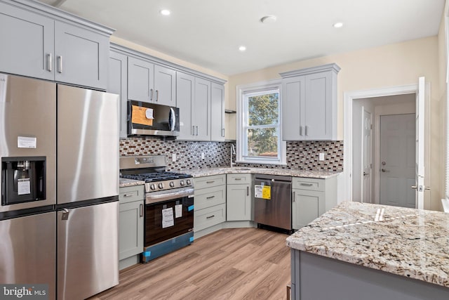 kitchen featuring backsplash, gray cabinetry, light hardwood / wood-style floors, and appliances with stainless steel finishes