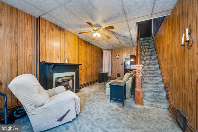 living room with carpet flooring, wood walls, and ceiling fan