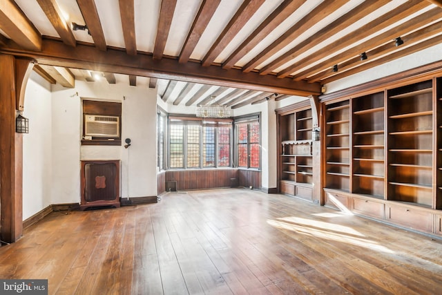 unfurnished living room featuring beam ceiling, wood walls, a wall unit AC, and hardwood / wood-style flooring