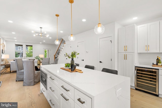 kitchen featuring pendant lighting, wine cooler, light hardwood / wood-style flooring, a kitchen island, and white cabinetry