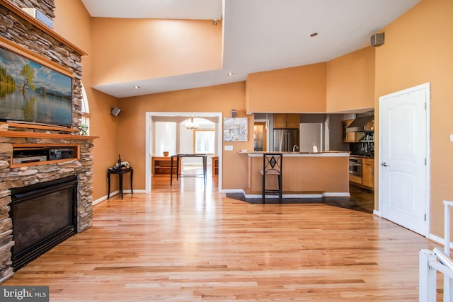 interior space with a stone fireplace, wall chimney range hood, light wood-type flooring, kitchen peninsula, and a breakfast bar area