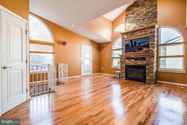 unfurnished living room with high vaulted ceiling, light hardwood / wood-style floors, and a stone fireplace