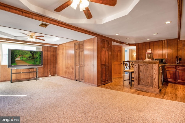 living room with light carpet, a tray ceiling, ceiling fan, and wooden walls