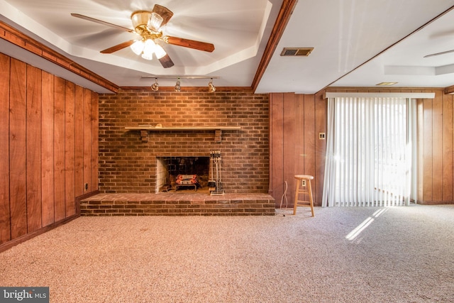 unfurnished living room with carpet floors, track lighting, a brick fireplace, and wood walls