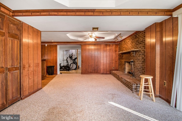 unfurnished living room with ceiling fan, wood walls, light colored carpet, and a fireplace