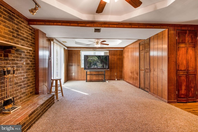 unfurnished living room featuring a raised ceiling, wood walls, light carpet, and track lighting