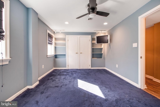 unfurnished bedroom with ceiling fan, track lighting, and dark colored carpet