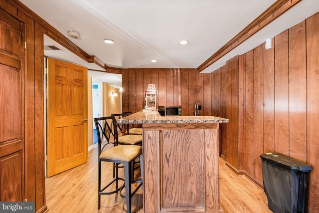 bar featuring light stone counters, light hardwood / wood-style flooring, crown molding, and wood walls