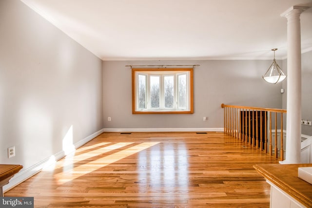 spare room featuring light wood-type flooring, ornate columns, and crown molding