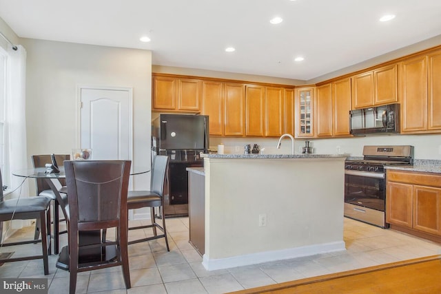 kitchen with light stone counters, a kitchen island with sink, sink, black appliances, and light tile patterned flooring