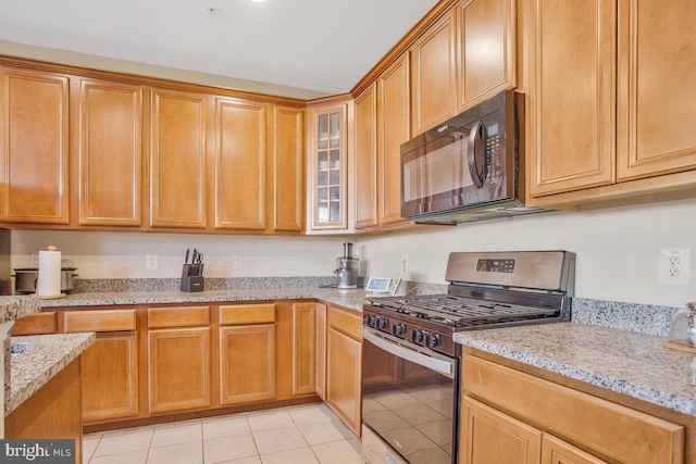 kitchen with stainless steel range with gas cooktop, light tile patterned flooring, and light stone countertops