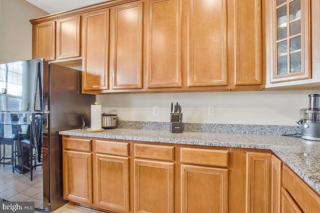 kitchen featuring light tile patterned flooring, black fridge, and light stone countertops