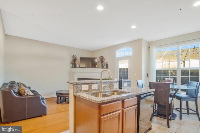 kitchen with a center island with sink, sink, light hardwood / wood-style flooring, stainless steel dishwasher, and light stone countertops