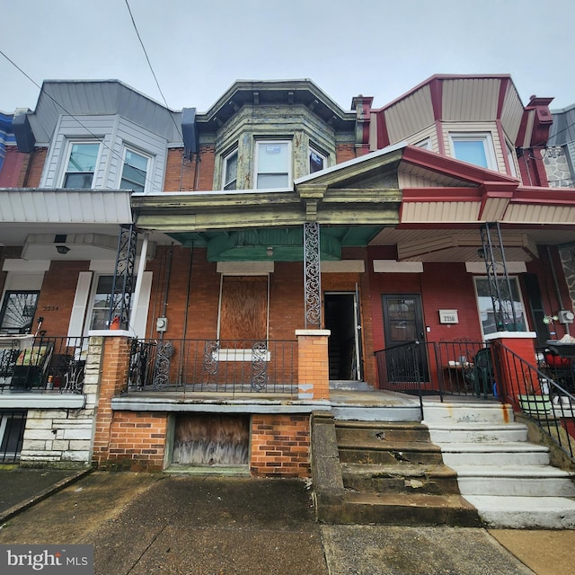 townhome / multi-family property featuring covered porch and brick siding