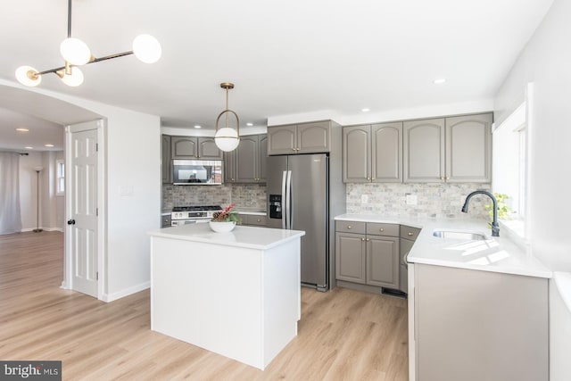 kitchen with sink, a center island, light hardwood / wood-style flooring, pendant lighting, and appliances with stainless steel finishes