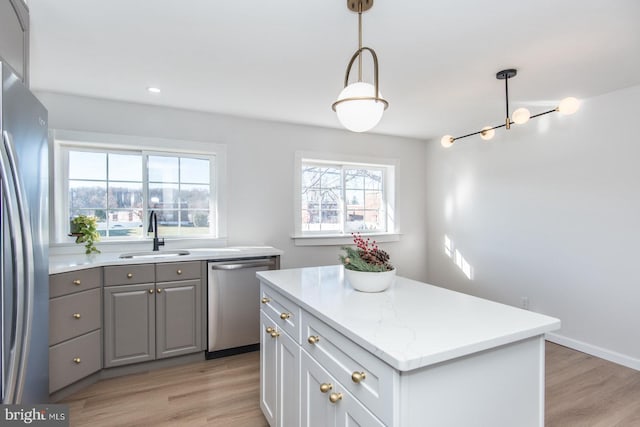 kitchen featuring sink, light hardwood / wood-style flooring, appliances with stainless steel finishes, decorative light fixtures, and a kitchen island