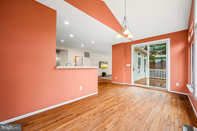 unfurnished dining area featuring light hardwood / wood-style floors, lofted ceiling, and a chandelier