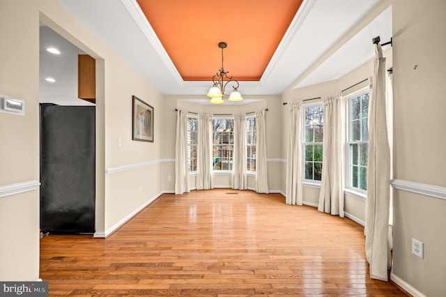 unfurnished dining area with light hardwood / wood-style floors, a raised ceiling, ornamental molding, and an inviting chandelier